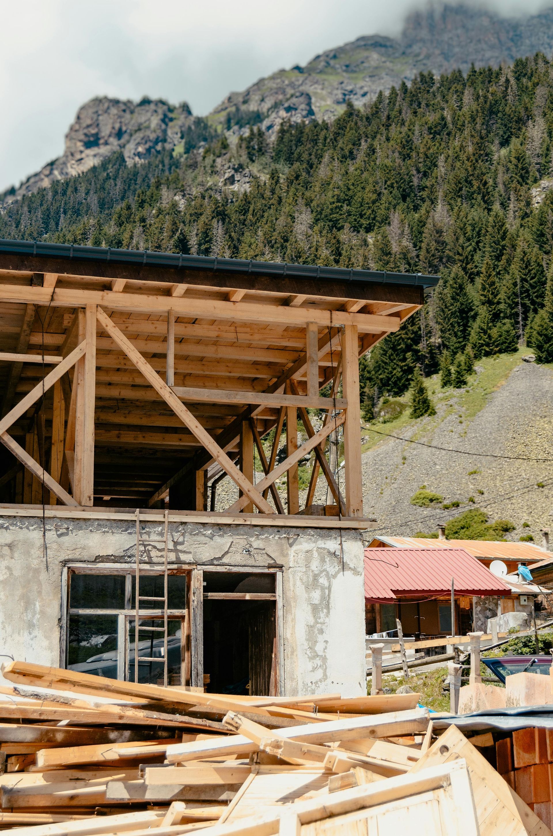 Partially built wooden structure with mountain forest backdrop and scattered lumber in foreground