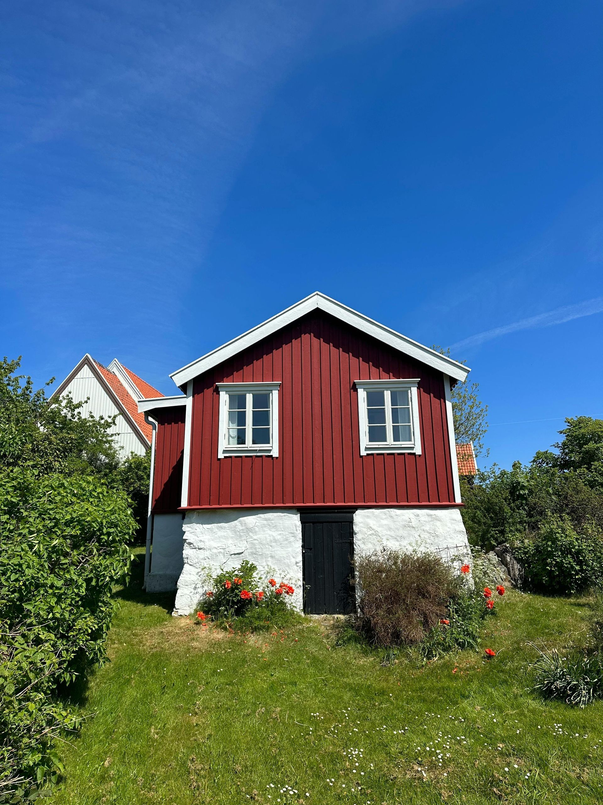 Red cottage with white-trimmed windows on a grassy hill under a clear blue sky