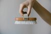 Hand holding a wooden brush with white bristles against a plain gray background