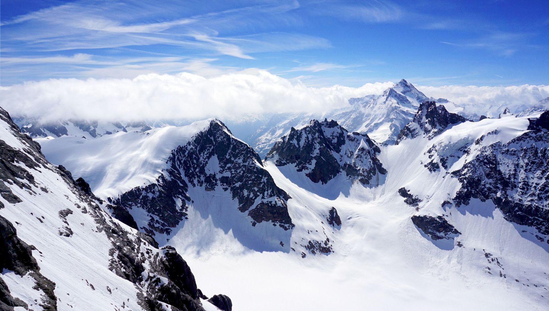 Cime montuose innevate che si ergono sopra una valle alpina avvolta dalle nuvole.