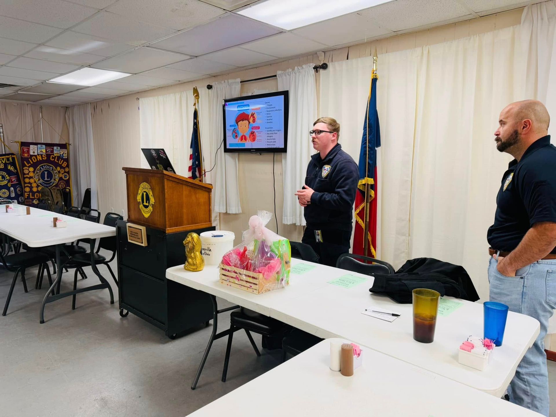 Two men are standing in a room with tables and a podium.