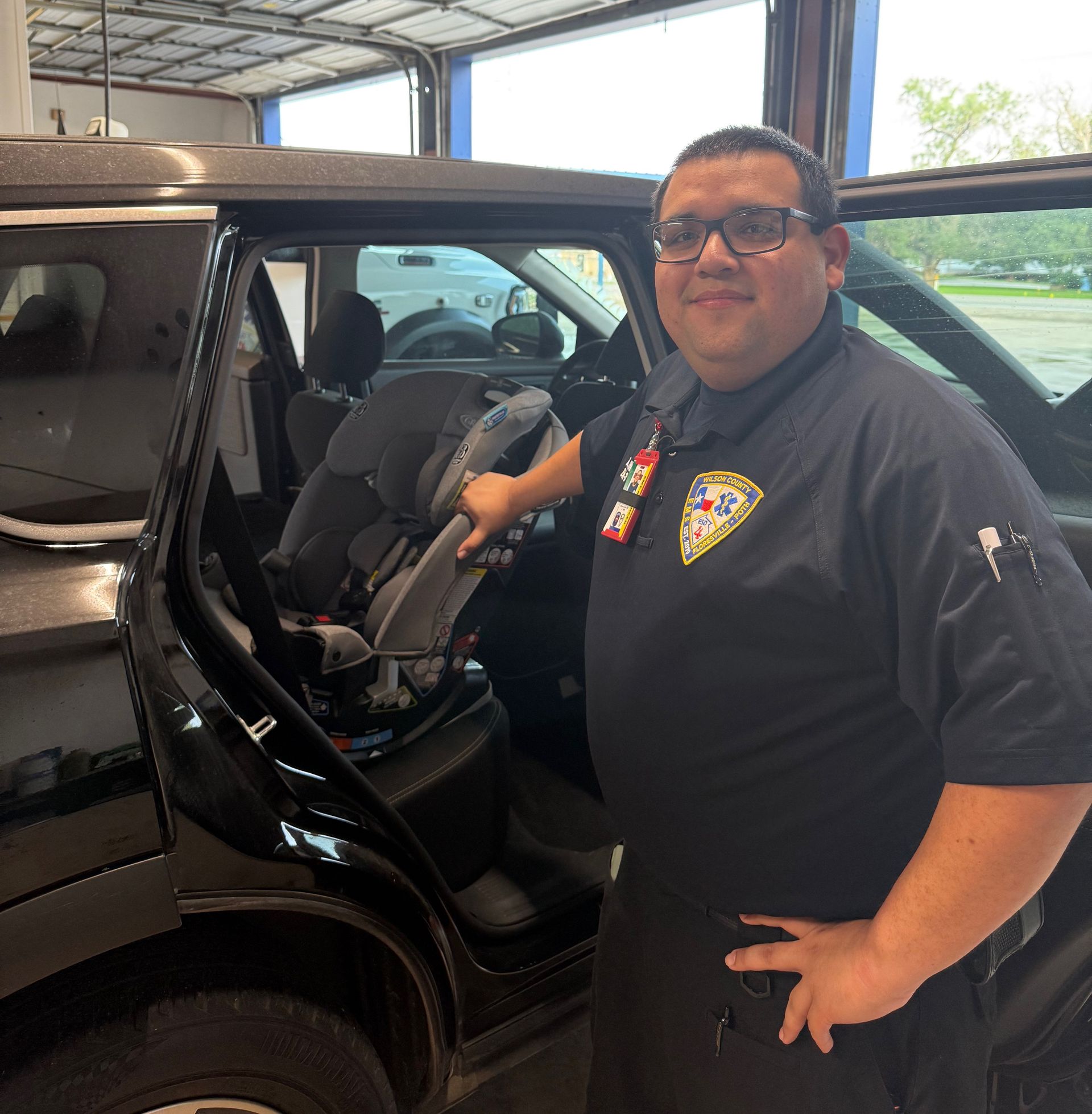 Man in uniform by a car with a car seat, smiling in a garage.