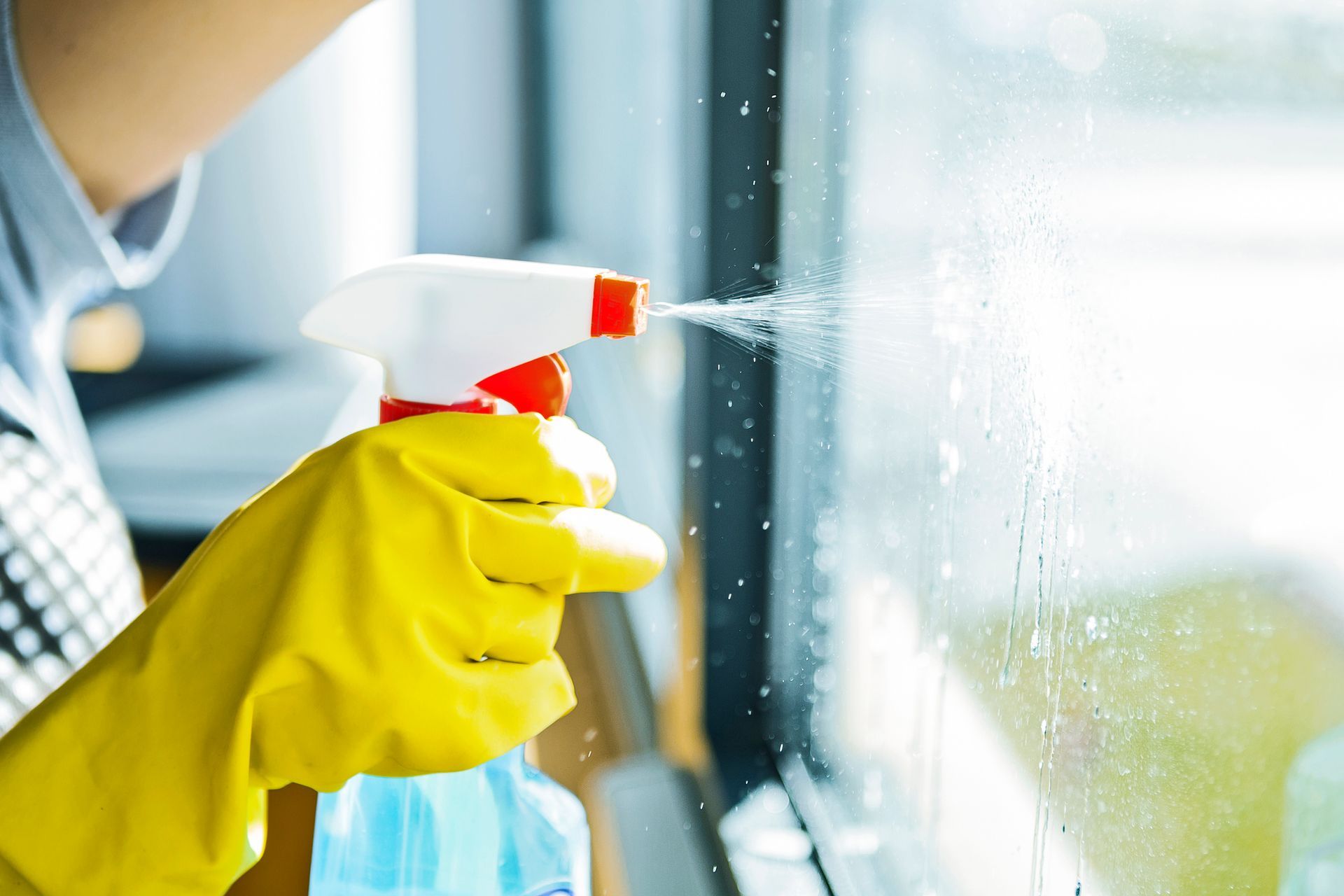 A person wearing yellow gloves is cleaning a window with a spray bottle.