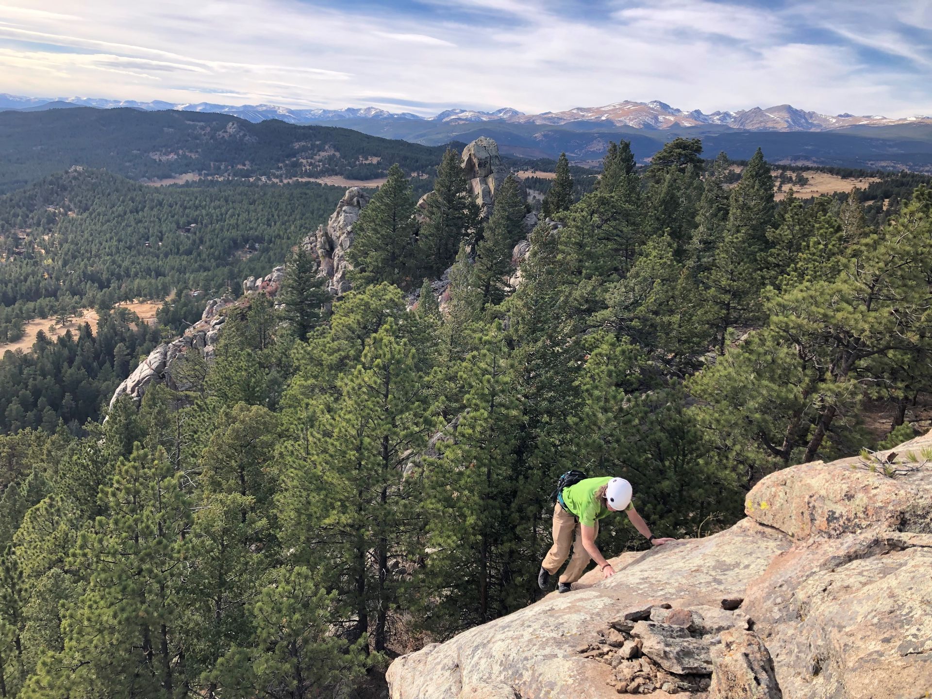 Person in green shirt and helmet rock climbing, with mountain views.