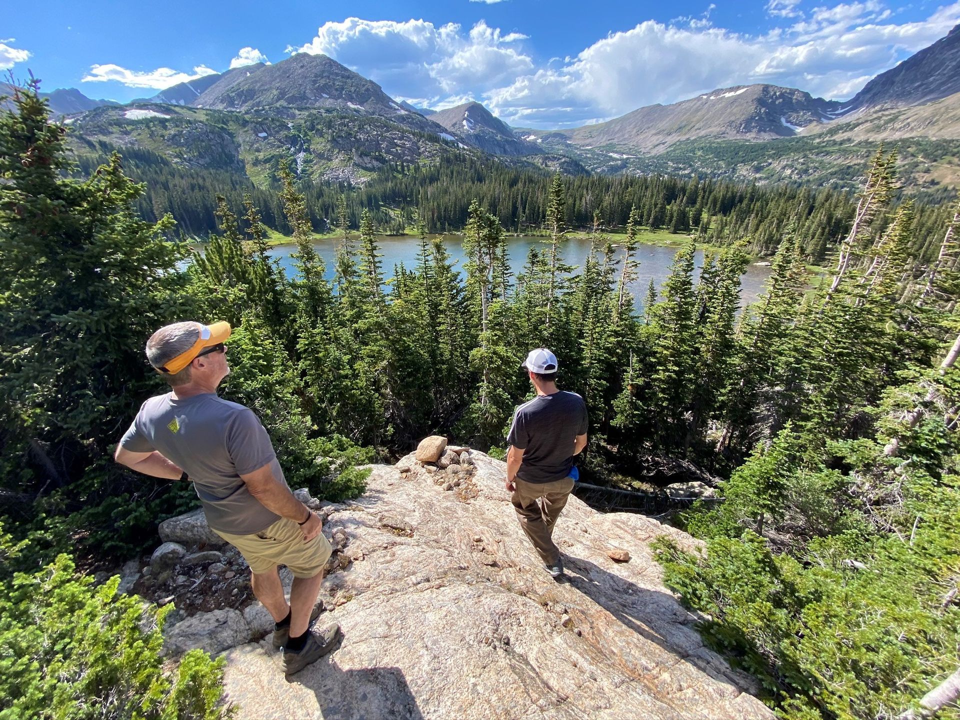 Two hikers overlook a mountain lake, sunny day.