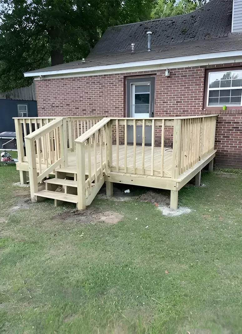 Small wooden wheelchair ramp and deck attached to a brick house in a grassy yard