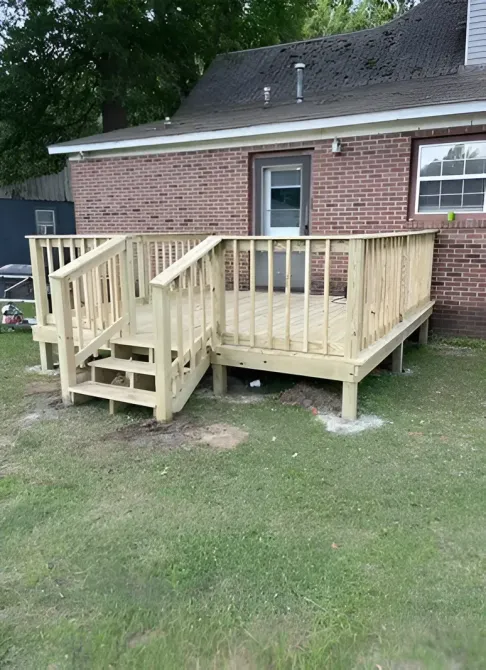 Small wooden accessibility ramp and deck attached to a brick house, with steps and railings.