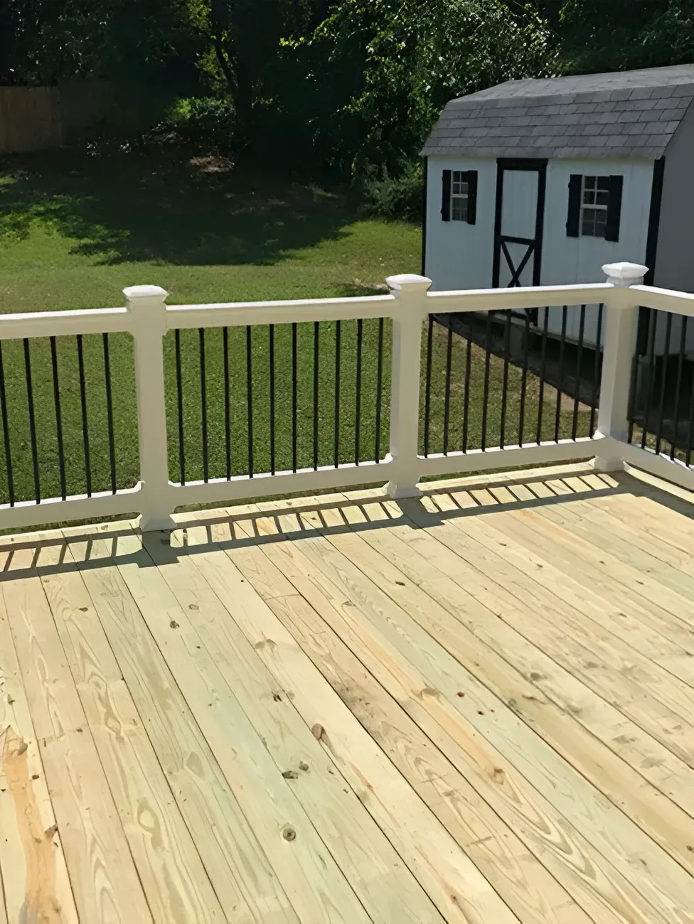 Wooden deck with white railing overlooking a green backyard and a small shed