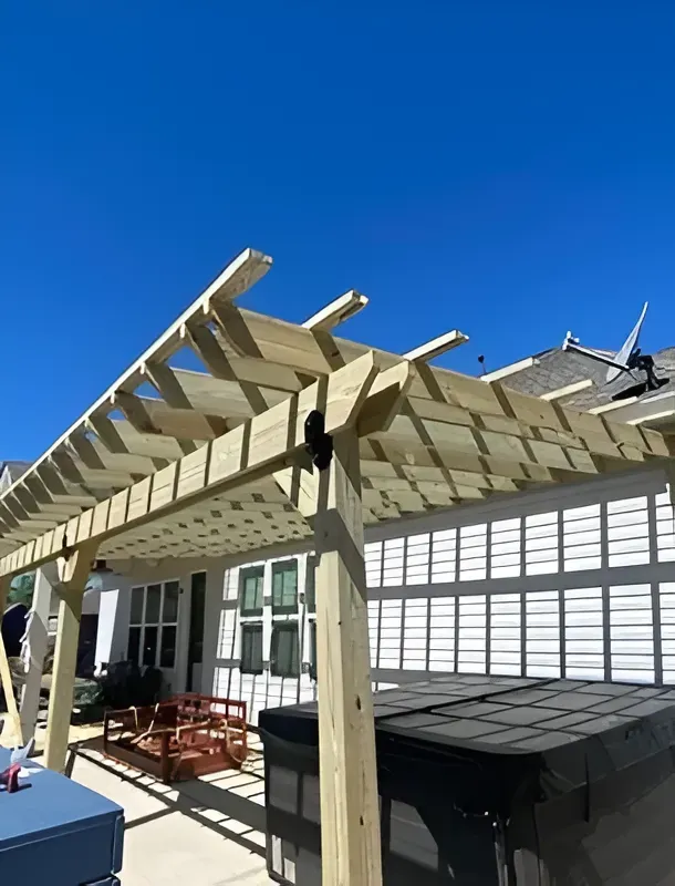 Patio pergola under construction beside a white house under a clear blue sky