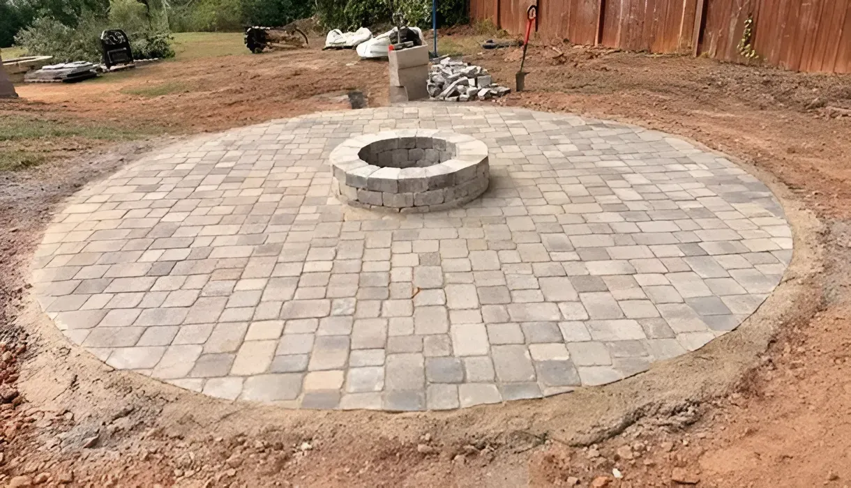 Brick-paved circular patio with a stone fire pit in a dirt yard