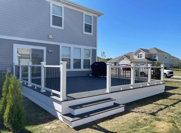 Backyard deck with white railings and steps beside a gray two-story house on a sunny day