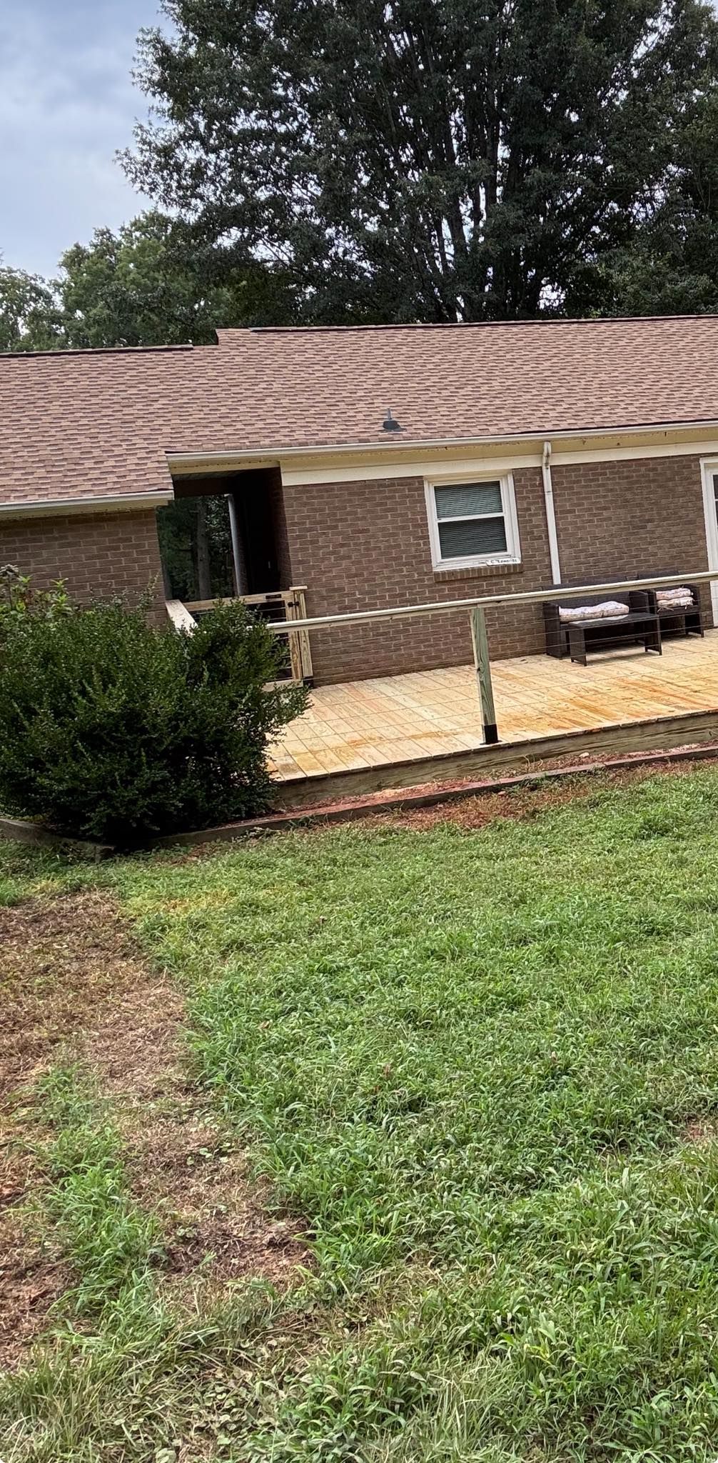 Backyard of a brick house with a stone patio, black chairs, and a green lawn under trees