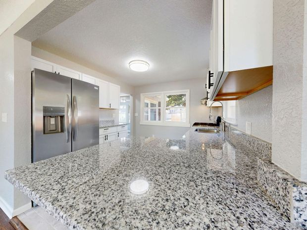 Bright modern kitchen with granite countertops, stainless steel refrigerator, white cabinets, and a window.