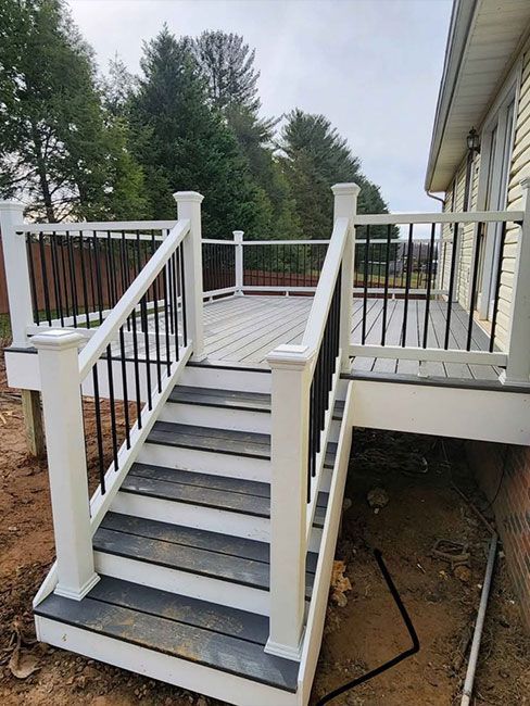 White wooden deck stairs leading to a porch, with railings and a house exterior beside them.