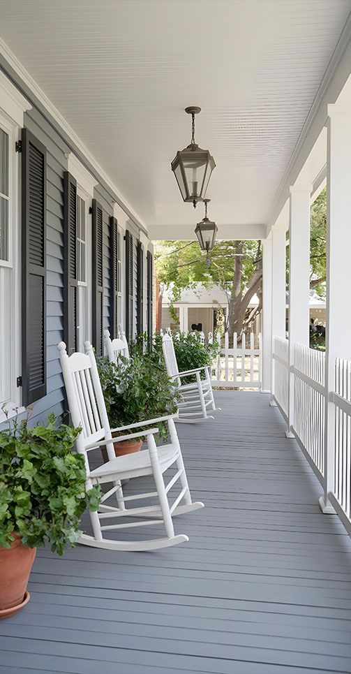 White rocking chairs on a gray porch with potted plants, shutters, and a hanging lantern.