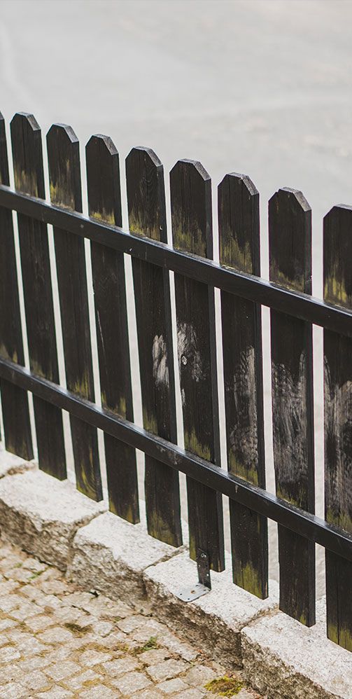 Black wooden picket fence along a cobblestone path beside a gray wall