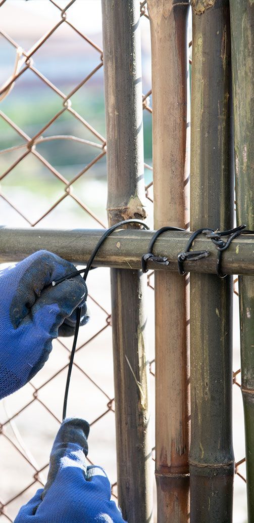 Gloved hands work on a wire fence gate, using tools to tighten the metal latch.