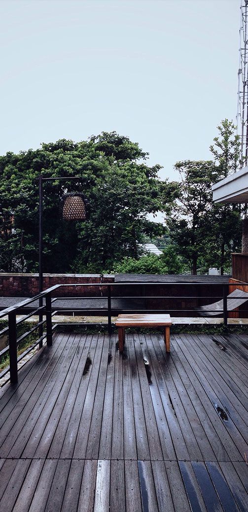 Rainy patio with wet wooden deck, glass railing, trees, and a small table and chairs outdoors