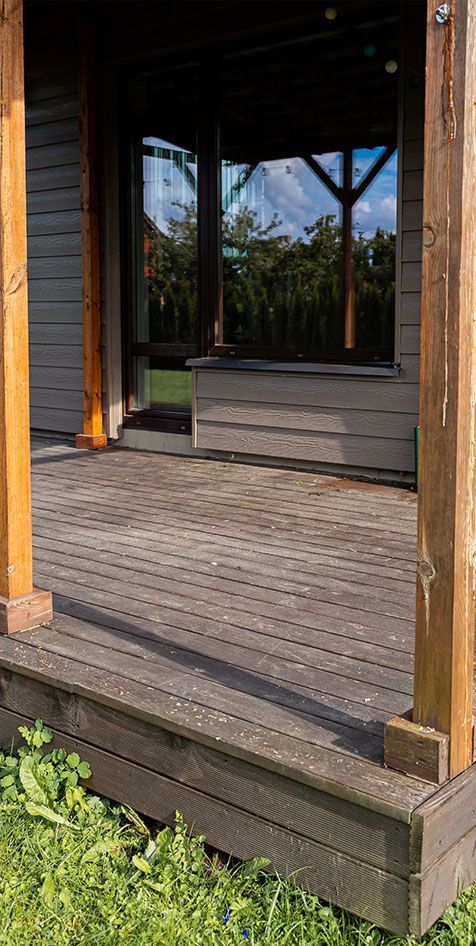 Wooden porch with open doorway, steps, and potted greenery in sunlight