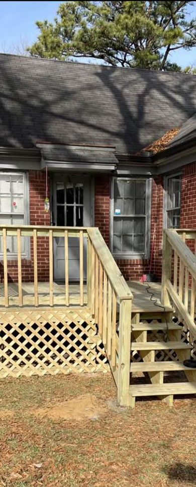 Front porch of a brick house with yellow wooden stairs and railing, shadowed by trees.