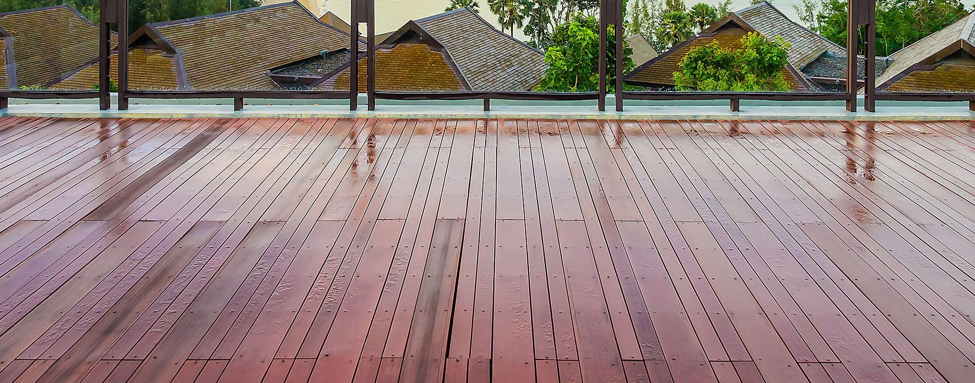 Wooden deck under a covered patio, with a garden and stacked branches beyond the railing.
