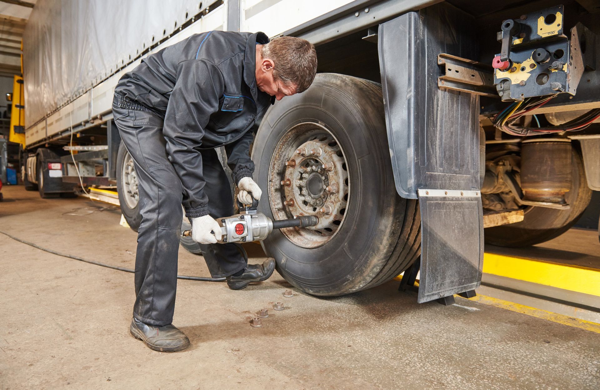 Mechanic tightening lug nuts on a truck wheel with a power tool in a garage