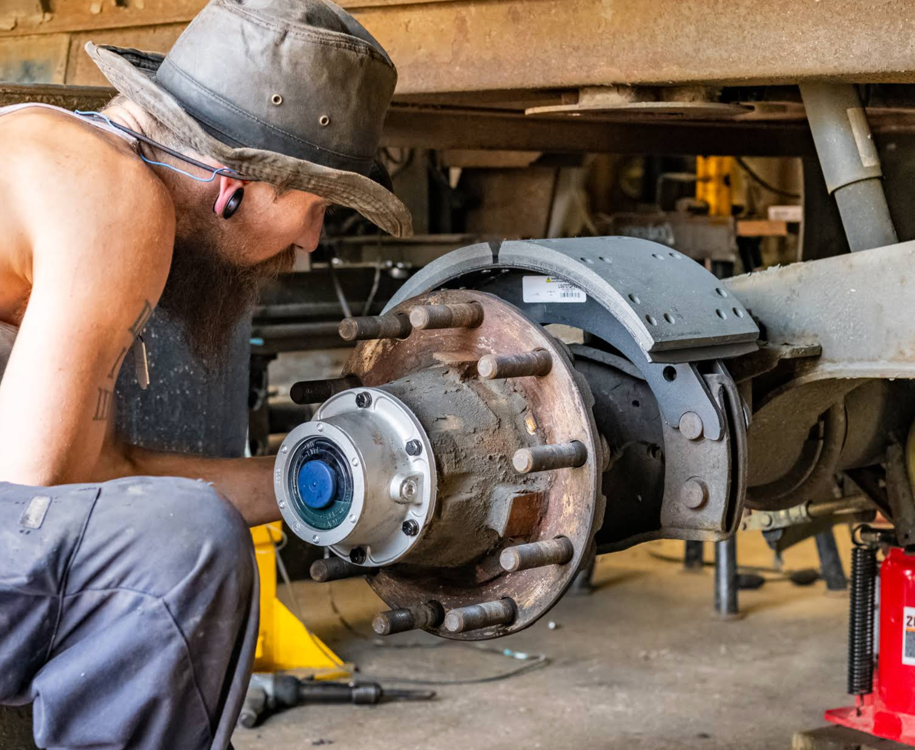Mechanic inspecting a truck wheel hub with tools under a raised vehicle in a garage