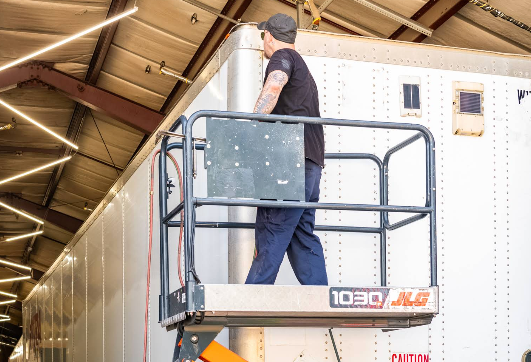Worker in a raised lift inspecting the ceiling inside a warehouse with exposed beams.