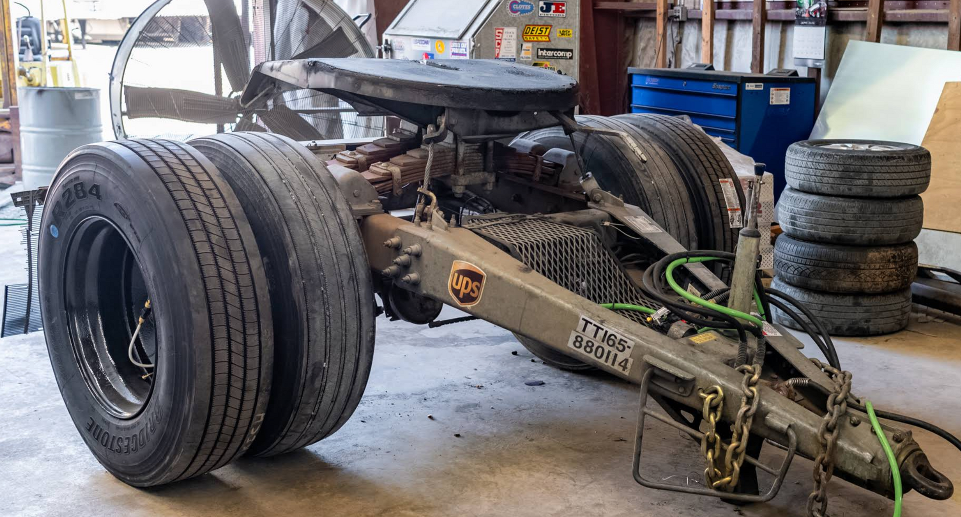 Truck chassis in a garage, with dual rear tires and a front axle exposed during repair.