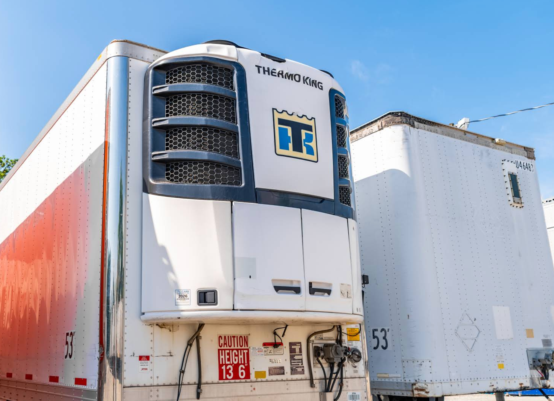 Refrigerated trailer trucks parked in a lot, one white unit with blue vents in front