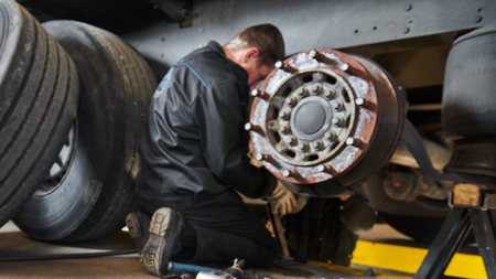 Mechanic inspecting a truck wheel hub with tools under the vehicle in a garage
