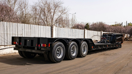 Black flatbed trailer with three rear axles parked on a snowy roadside, side view