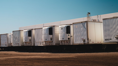 Row of white refrigerated freight trailers parked on a rail siding in a dry industrial yard