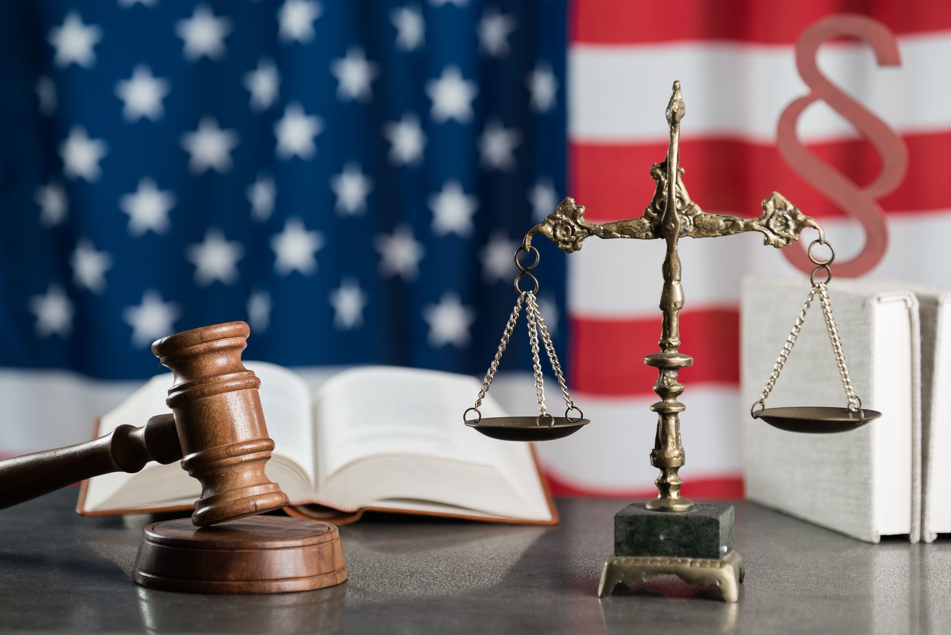 Judge’s gavel, justice scales, open law book, and U.S. flag in a courtroom scene