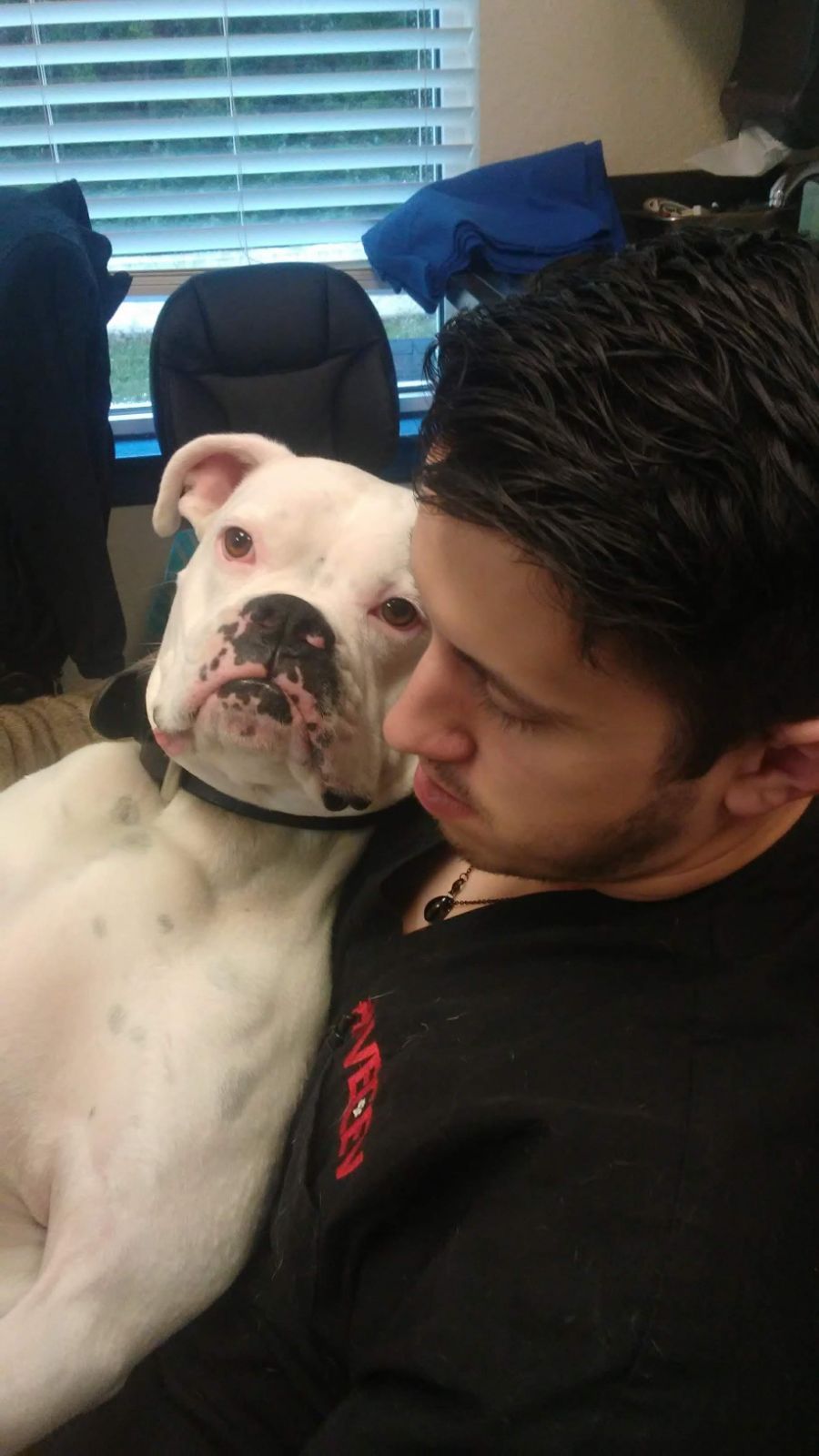 Man cuddling a white dog in a home office, both resting close together on a chair
