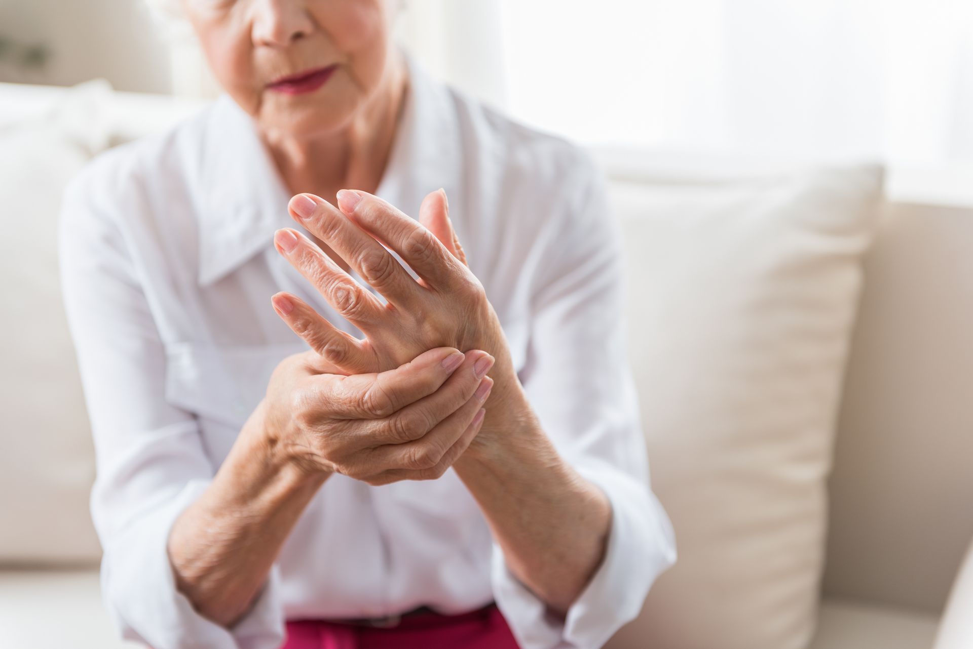Woman in a white blouse rubbing her painful wrist on a couch