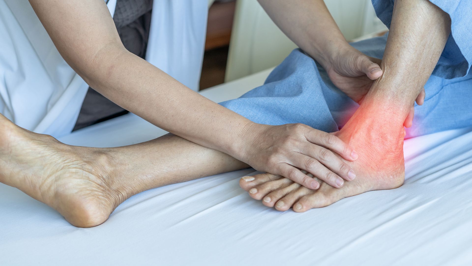 Physiotherapist holding a patient's painful ankle with red highlight on a treatment bed