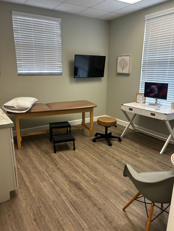 Small exam room with two desks, computer monitors, stools, and wall-mounted TV.