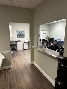 Office reception area with granite counter, water cooler, desks, and a hallway to a back room.