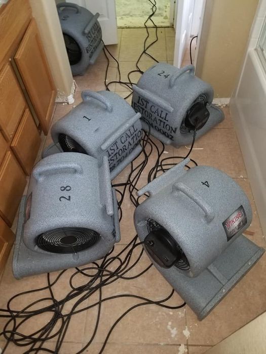 Several gray portable fans scattered on a tiled floor, with tangled black cords in a room.