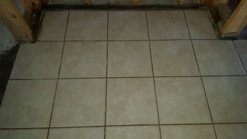 Beige tiled floor beneath wooden furniture legs, viewed from above.