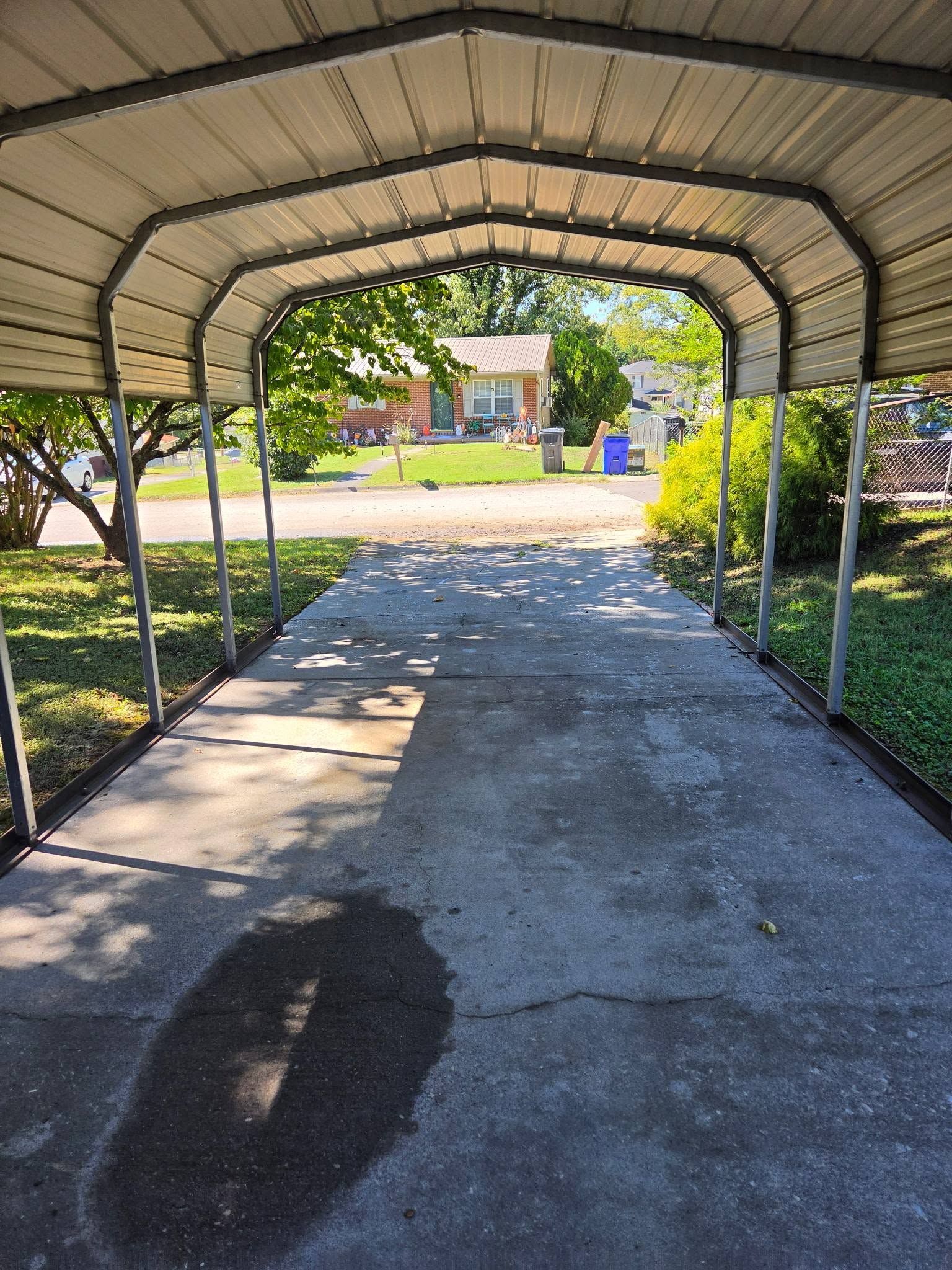 Covered driveway leading to a house, with trees and bushes on either side.