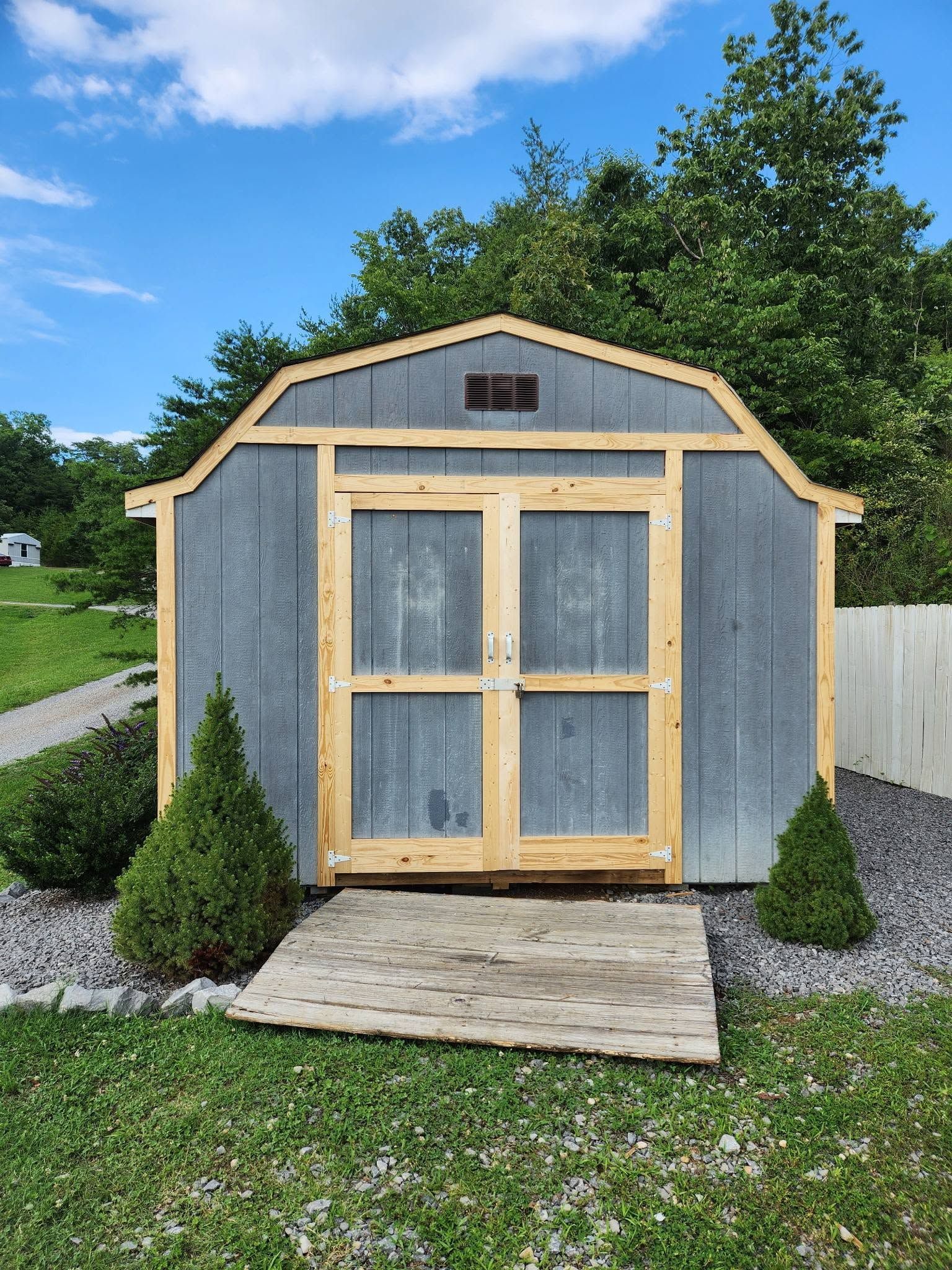 Gray garden shed with light wood trim, double doors, and a small ramp in a grassy yard