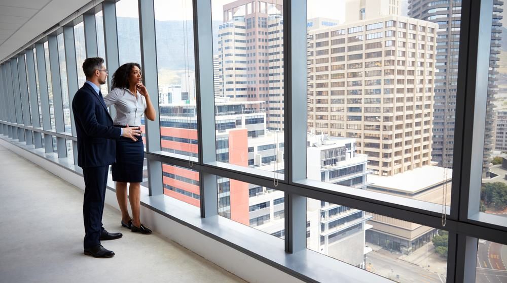 A man and a woman are looking out of a window at a city.