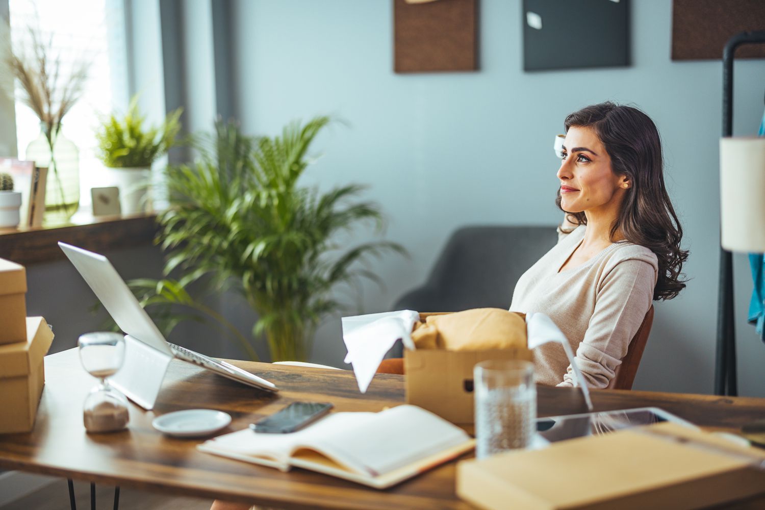 A woman is sitting at a desk with a laptop and boxes.