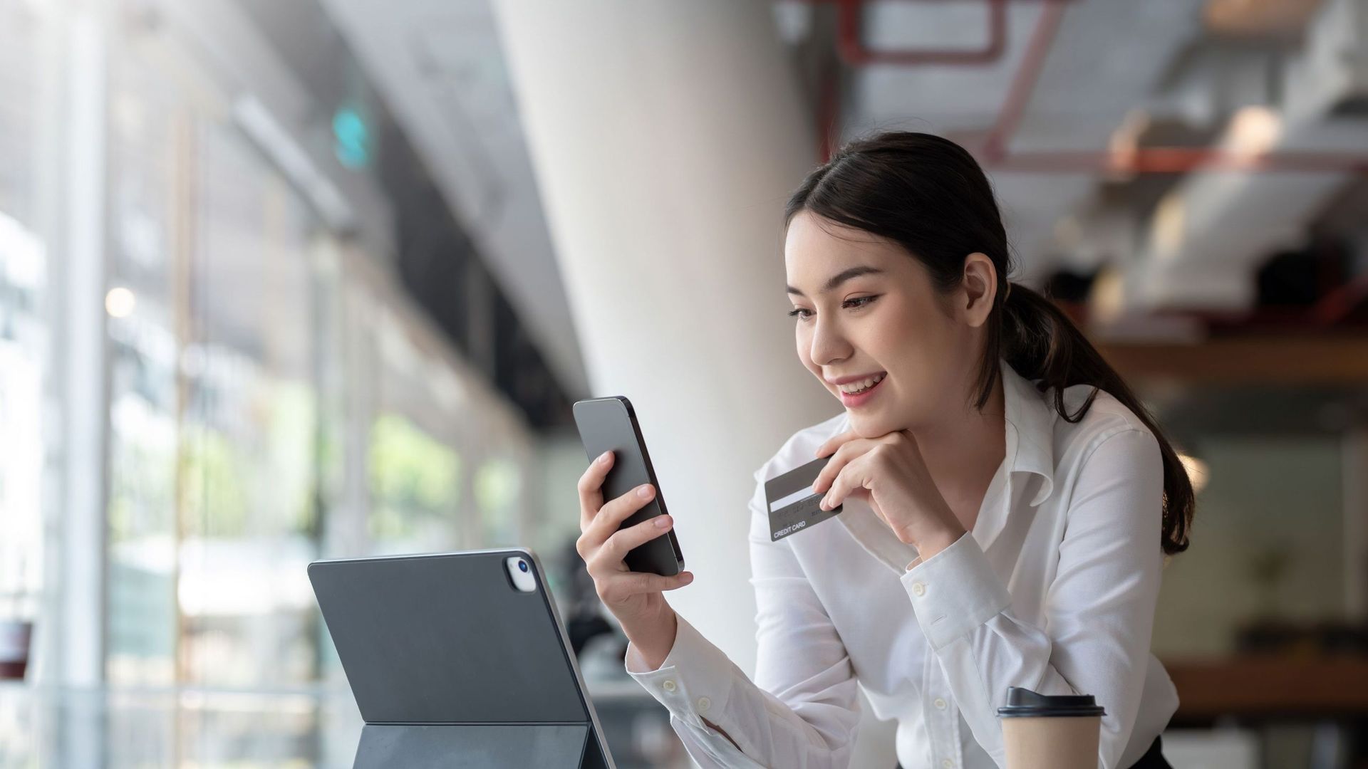 A woman is sitting at a table using a tablet and a credit card.