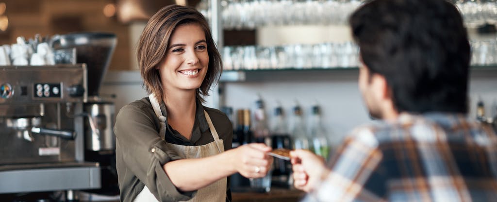 A woman is giving a credit card to a man in a restaurant.