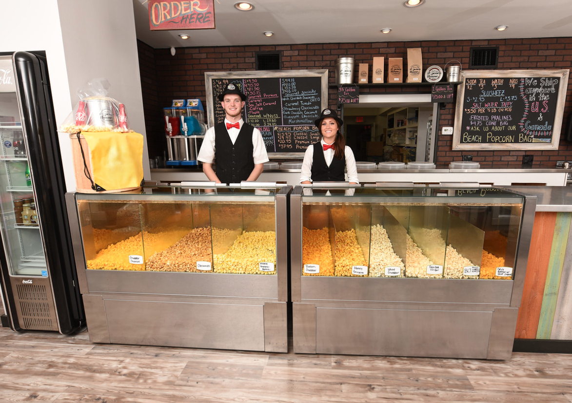Popcorn counter with two staff behind glass display cases of popcorns