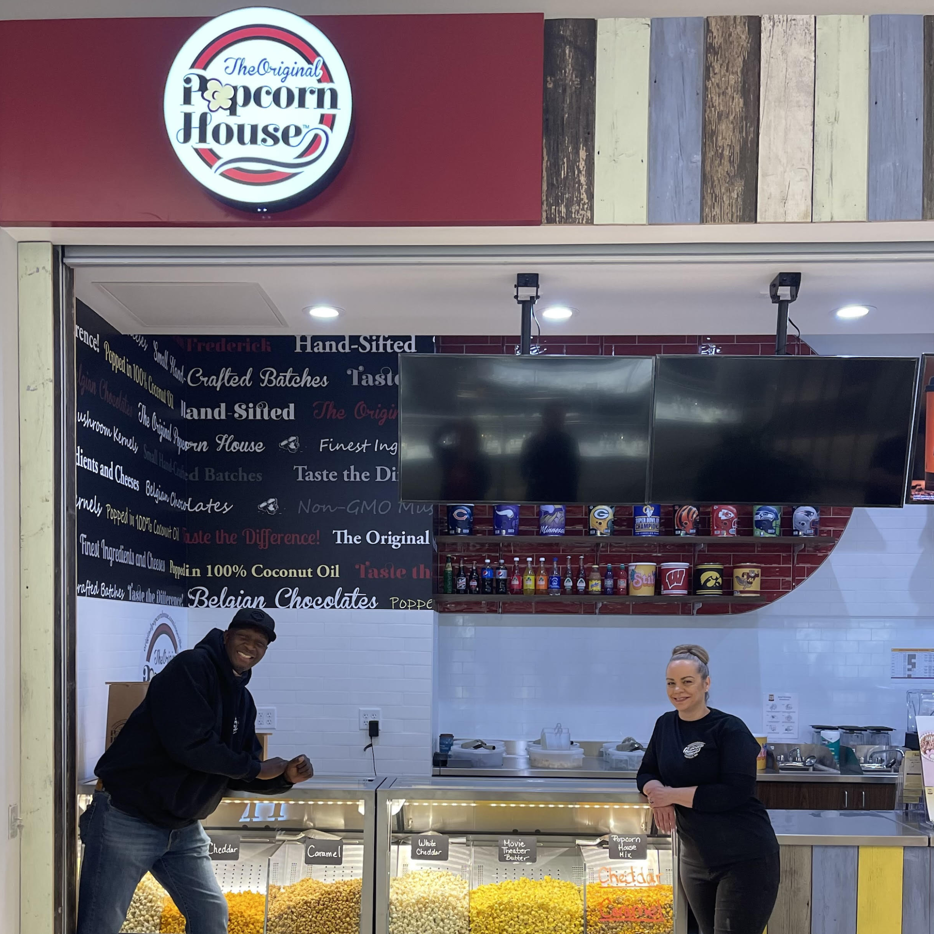 Two people behind a popcorn counter with a large menu board and Popcorn House sign above.