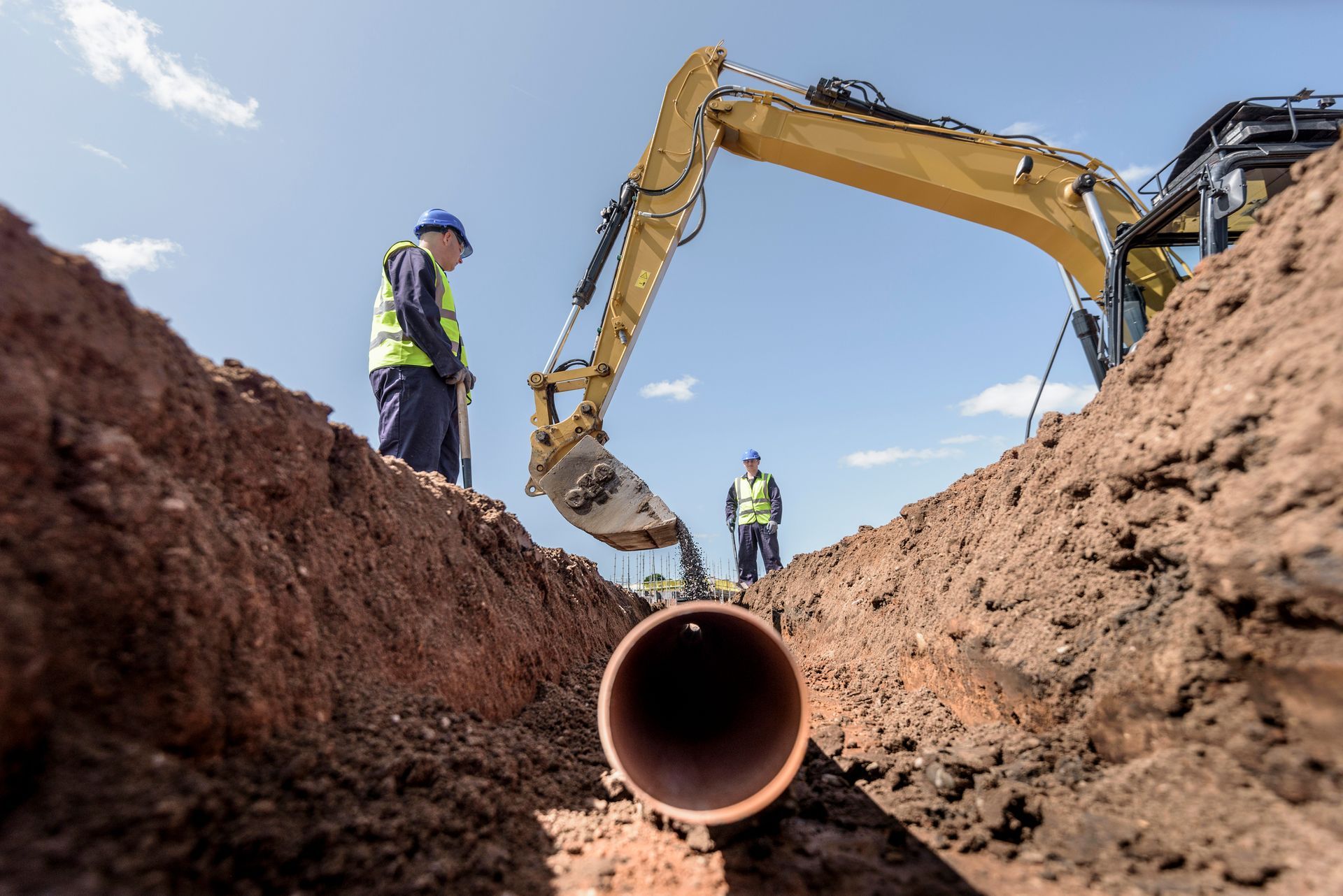 A man is standing in a trench looking at a pipe being installed.